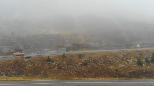 Tiro aéreo de carro laranja andando pela estrada da montanha no outono. Auto condução na rota nebulosa do campo. SUV movendo-se através da paisagem cênica maneira na bela temporada. Conceito de viajar. Vista superior — Vídeo de Stock