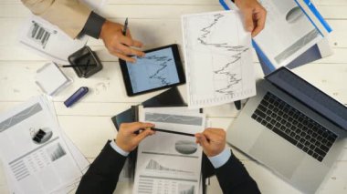 İki başarılı iş ortağının erkek elleri grafikleri inceler ve ofiste finansal raporları tartışırlar. Genç işadamları masada oturuyor ve yeni bir iş projesi geliştiriyor. Üstte görüntü