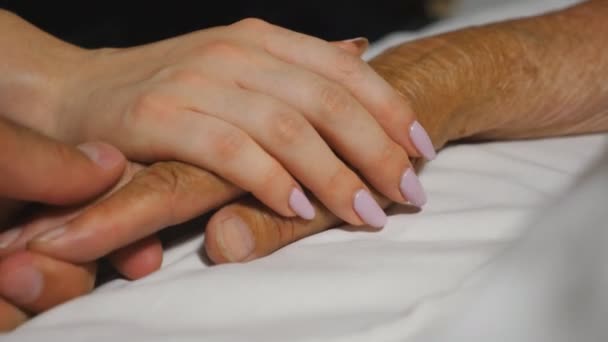 Бабуся і онук м'яко погладжують руку своєї бабусі, лежачи в лікарні на ліжку. Молода жінка і чоловік комфортно зморшкував руку хворої бабусі в медичній клініці. Поняття турботи і любові. крупним планом — стокове відео