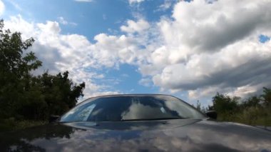 Siyah araba kırsaldan geçiyor. Kaputta yansımaları var. Gökyüzü ve bulutlardan oluşan bir pencere. Otomobille otoban boyunca güzel manzaranın içinden geçmek. Kaputtan ön cama bak