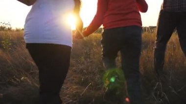 Anne ve baba ve iki çocuk el ele tutuşup gün batımında çim tarlasında koşuyorlar. Çayırlarda koşan ve kollarını kaldıran çocuklu mutlu ebeveynler. Aile tatili kavramı