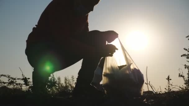 Close up of little male kid in gloves collect trash in bag saving nature at countryside. Parents of boy help to cleaning lawn of paper waste at background. Concept of environmental problem. Slow mo — Stock Video