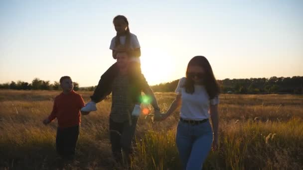 Mama und Papa mit kleinen Kindern auf dem Weg durch die Wiese. Ein junges Elternpaar mit zwei Kindern geht bei Sonnenuntergang auf einer Wiese spazieren. Glückliche Familie, die zusammen Zeit in der wunderschönen Natur verbringt. Nahaufnahme — Stockvideo