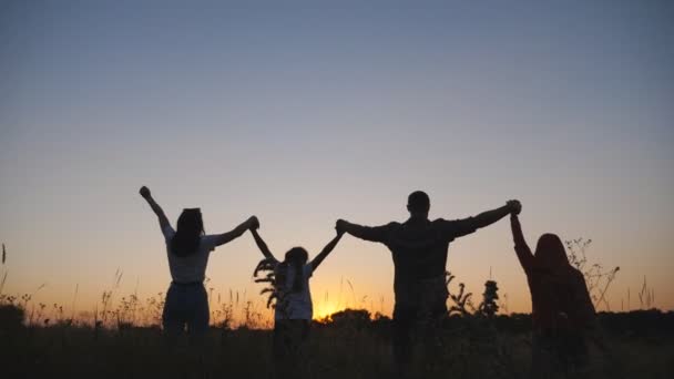 Мать и отец с двумя маленькими детьми стоят на травяном поле с поднятыми руками на закате. Счастливая молодая семья любит проводить время вместе на природе. Понятие беззаботности и свободы. Долли выстрелил — стоковое видео