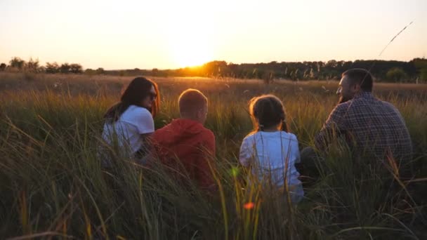 Молодые родители с маленькими детьми проводят время вместе на лугу. Мама и папа с двумя детьми сидят на траве на поле и наслаждаются отдыхом на природе. Понятие семейного счастья. Долли выстрелил — стоковое видео