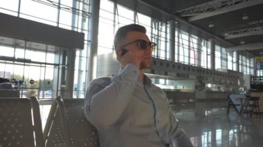 Genç ciddi iş adamı havaalanında telefonda konuştu ve konuşmayı tamamladı. Ofiste cep telefonundan konuşan güneş gözlüklü yakışıklı beyaz iş adamı portresi. Yavaş çekim