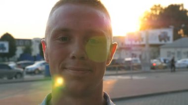 Seyir ve fotoğraf makinesi ile duygu ve duygular içine günbatımı üzerinde gülümseyen genç mutlu işadamı portresi. Arka plan, güneş ışığı ile caddenin üzerinde gömlek duran emin yakışıklı adam. Yakın çekim