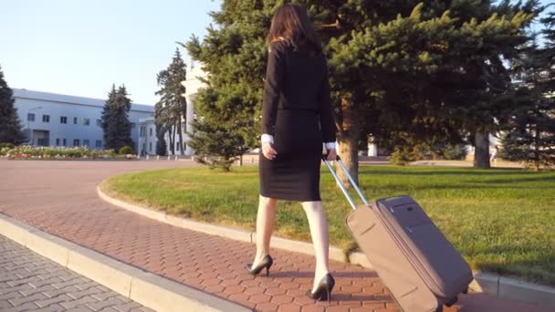 Onherkenbare zakenvrouw met koffer loopt naar het vliegveld om op zakenreis te gaan. Dame met hoge hakken stapt met haar bagage langs straat. Reisconcept. Achteraanzicht Langzame beweging Close up — Stockvideo