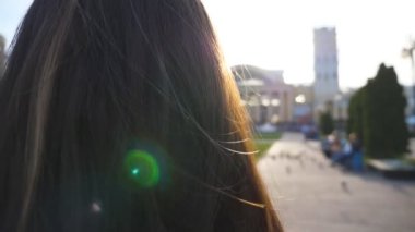 Yaz güneşli bir gün kentsel sokakta yürüyüş genç kadın saç. Kız saç ile oynarken esinti zevk. Kız arka planda parlak güneş ışığı ile kaldırım adım. Arka görünüm yakın çekim