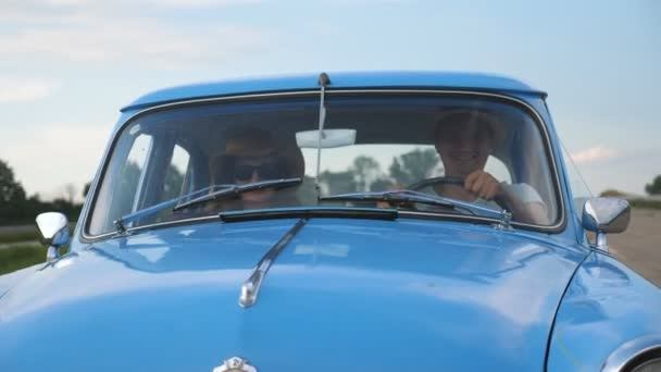 Młoda uśmiechnięta para w kapeluszach jadąca w zabytkowym samochodzie podczas letnich podróży. Szczęśliwy mężczyzna i kobieta siedzący na przednim siedzeniu starego samochodu retro i cieszący się jazdą i wakacjami. Koncepcja podróży. Zwolniony ruch — Wideo stockowe