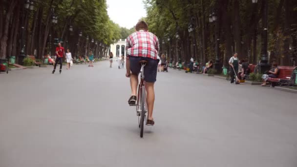 Young man riding a vintage bicycle at alley of public park. Sporty guy cycling outdoor. Healthy active lifestyle. Back view Close up Slow motion — Video Stock