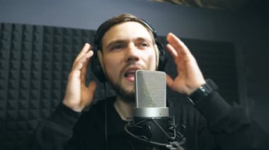 Duygusal olarak kayıt yeni melodi veya şarkı genç adam. Erkek şarkıcı şarkı ses stüdyosunda mikrofona kulaklık. Yaratıcı müzisyen çalışma. Haritayı iş kavramı. Ağır çekim