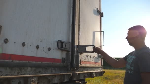 Driver opens the doors on trailer of parked truck. Lorry stopped in the countryside. Beautiful landscape at background. Side view Slow motion Close up — Vídeo de Stock