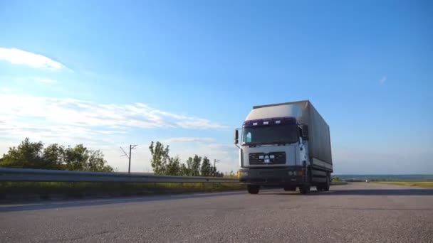 Kamera podąża za ciężarówką jadącą autostradą. Ciężarówka przejeżdża przez wieś z pięknym krajobrazem w tle. Widok z boku Spowolnienie ruchu — Wideo stockowe