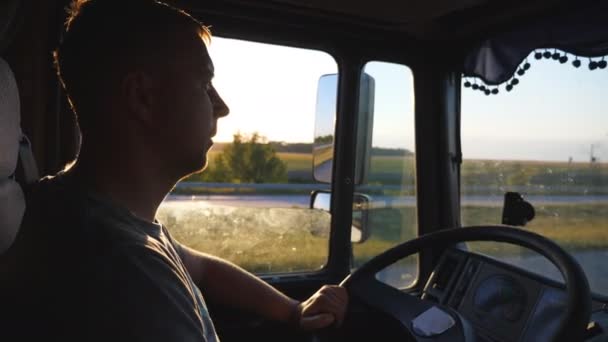 Muž řídit náklaďák a pečlivě sledovat silnici. Kavkazská chlap je jízda krajinou na slunce pozadí. Profil z řidiče uvnitř kabiny. Boční pohled zpomalené Detailní záběr — Stock video