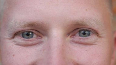 Mavi gözlü bir adamın mutlu bakışları ve göz kırpışları. Erkek yüzünün pozitiflikle kameraya bakışının portresi. Gülümseyen genç adamın yüz ifadesi. Kapat.