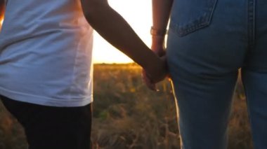 Gün batımında çayırda yürürken anne ve kızının kadın ellerine yakın olmak. Anne yazın çim tarlasında çocukla yürüyor. Arka planda güzel bir güneş ışığı var. Aile sevgisi kavramı