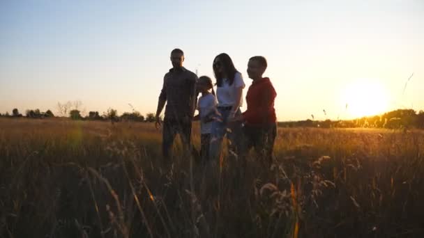 Mother and father with small kids walk through grass field holding hands of each other at sunset. Happy young family with two children going among summer meadow and enjoy to spending time together — Stock videók