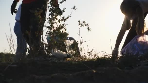 Närbild av små barn i handskar samla skräp i påsar rädda naturen på landsbygden. Föräldrar till barn hjälper till att rengöra gräsmattan av pappersavfall i bakgrunden. Begreppet miljöproblem. Långsam rörelse — Stockvideo