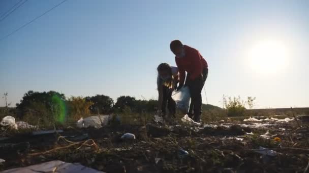 Little sister and brother in gloves collecting trash in bag at countryside. Small eco activists in protective masks cleaning lawn of trash near roadside. Concept of environmental problem. Dolly shot — Stock Video