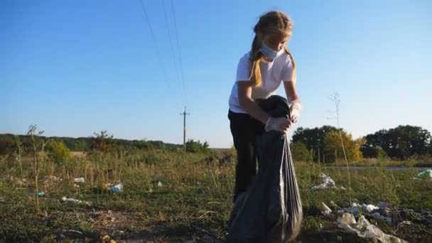 Small bad girl in gloves taking big bag with garbage and carrying it on landfill at nature. Little female child polluting environment at countryside. Concept of social issues and ecological problem — Stock Video