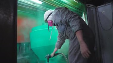 İşçiler boya odasındaki spreyden metal parçalarına boya sıkarlar. Endüstriyel imalatta güvenlik görevlisi. Uzman atölyede usta boya detayı. Yavaşça kapat.