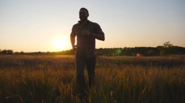 Close up of happy man running through grass field with sunset at background. Young guy jogging among summer meadow. Male enjoying rest at beautiful nature. Concept of carefree and freedom. Slow mo