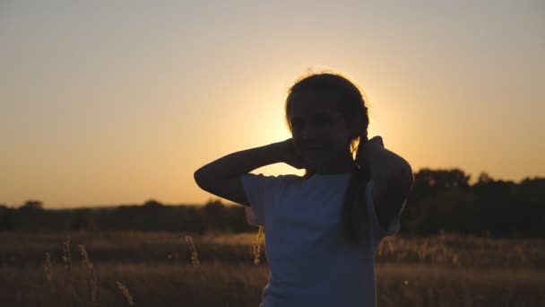 Close up of little smiling girl look into camera standing in meadow and playing with her hair. Portrait of happy small child in grass field over sunset background. Concept of carefree and freedom — Video Stock