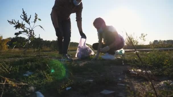 田舎の紙の廃棄物の若い父親と小さな娘の掃除牧草地。道端近くの芝生の芝生でゴミを集めるマスクのエコボランティアの家族。自然を守るという概念。ドリーショット — ストック動画