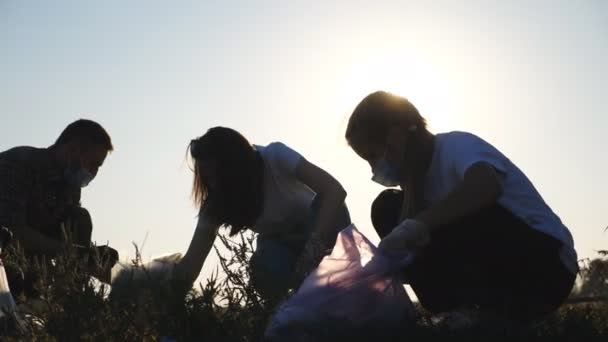 Young parents and their daughter in gloves collecting trash in bags near roadside. Family of eco activists in masks clean lawn of paper waste saving nature. Concept of environmental problem. Close up — Stock Video