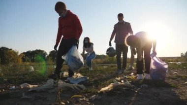 Maskeli, plastik ve kağıt atığı temizleyen çevre gönüllüleri ailesi doğayı koruyor. Genç ebeveynler ve eldivenli iki çocuk yol kenarında çöp topluyor. Çevresel bir sorun. Dolly vurdu.
