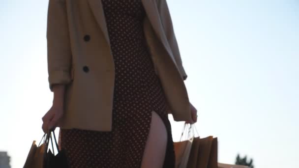 Κοντά στα χέρια της νεαρής γυναίκας μεταφέρουν τσάντες ψώνια με τα πόδια κατά μήκος του αστικού δρόμου. Γυναικεία όπλα κρατούν χάρτινα πακέτα που πηγαίνουν στο δρομάκι της πόλης μετά τις αγορές. Έννοια των πωλήσεων και των εκπτώσεων. Αργή κίνηση — Αρχείο Βίντεο