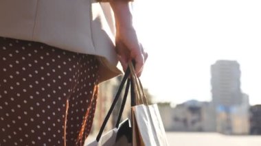 Alışveriş yaptıktan sonra alışveriş torbaları taşıyan genç bir kadın var. Kadın kolu, şehir caddesinde yürürken dolu kâğıt paketler tutuyor. Mevsimsel satış kavramı. Yavaş çekim