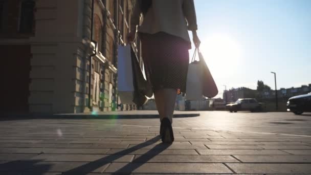Genç bayan müşteriler alışverişlerden sonra kaldırımda yürürken alışveriş torbalarını tutarlar. Şık bir kadın şehir meydanında kağıt paketler taşıyor. Boş zaman ve boş zaman kavramı. Arka plan Yavaş çekim — Stok video