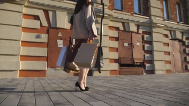 Femme à la mode porte des paquets de papier allant le long de la rue urbaine. Jeune fille tient sacs marchant sur le trottoir après les achats. Concept de ventes saisonnières et réductions. Dolly shot Mouvement lent — Video