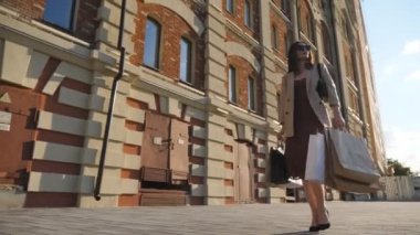 Çekici kadın şehir caddesinde yürüyen kağıt paketler taşıyor. Zarif genç kız alışveriş sonrası kaldırıma çıkan alışveriş torbalarını tutuyor. Mevsimlik satış ve indirim kavramı. Yavaş çekim