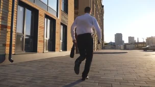 歩道上の正式な摩耗ジョギングで成功したマネージャー。都市部を走るブリーフケース付きの若いビジネスマン。会社員は遅刻します。男性起業家は働くのを急いでいる。ドリーショット — ストック動画