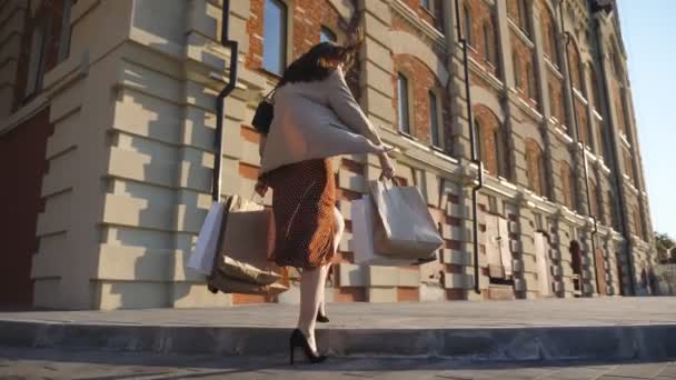 Elegante ragazza tiene borse della spesa in corso sul marciapiede dopo gli acquisti. Donna elegante porta pacchetti di carta a piedi lungo la strada urbana. Concetto di saldi stagionali e sconti. Dolly ha sparato a Lento mo — Video Stock