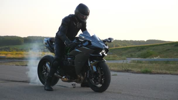 Un motard qui brûle des pneus avec beaucoup de fumée. Roue de moto sont glissant sur la route pendant le début du mouvement. Roue de moto sport commence à tourner à la route asphaltée. Mouvement lent Fermer Vue latérale — Video