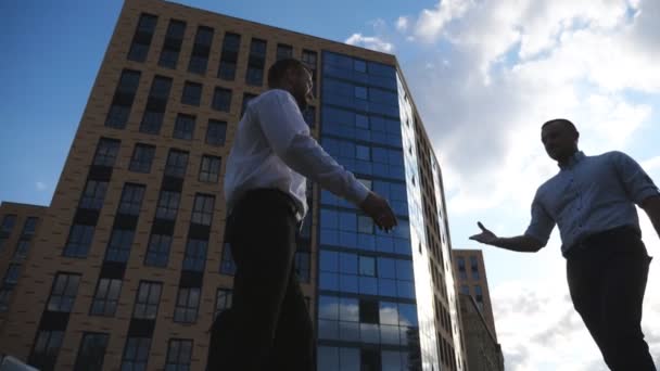 都市部と握手で正式な摩耗会議で2人の成功したマネージャー。若いビジネスマンはオフィスビルの近くの彼のパートナーに黒いブリーフケースを渡します。取引の概念。ドリーショットスローモ — ストック動画