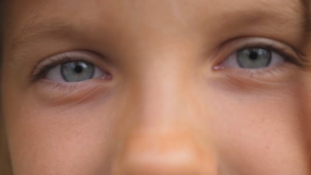 Blue eyes of beautiful small girl blinking and looking into camera with a sad sight. Portrait of cute face of young child watching with sorrowful expression. Close up — Stock Video