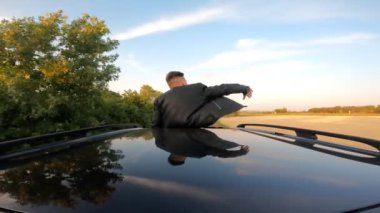 Arabanın sunroof 'unda duran ve kır yolunda giderken rüzgarla oynayan genç adam. Tanınmayan bir adam yolculuk ve esintinin tadını çıkarıyor. Seyahat ya da özgürlük konsepti. Arka plan