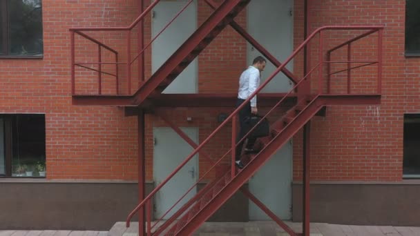 Zakenman klimt de trap op van een zakencentrum. Zelfverzekerde man in formele kleding met een tas die de trap oploopt en telefoneert. Werknemer pendelt naar zijn werk. Begrip succesvolle loopbaan — Stockvideo