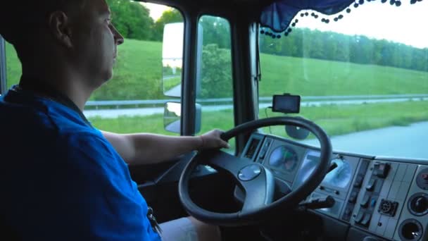 Profil uśmiechniętego kierowcy ciężarówki jadącego przez wieś o zachodzie słońca. Szczęśliwy człowiek kontrolujący swoją ciężarówkę i cieszący się podróżą. Widok wewnątrz kabiny ciężarówki. Strzał w środku Powolny ruch Zamknij — Wideo stockowe