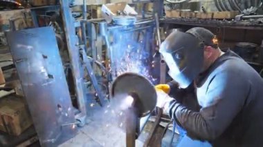 Endüstriyel üretimde koruyucu maske kaynak işçisi. Adam metal parçalarını birbirine kaynaştırıyor. Kaynakçı iki çelik detay arasında ortaklık yapıyor. Atölyede el emeği
