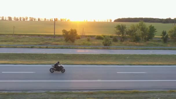Vista aérea para passeios de motociclista na moderna moto esporte na rodovia. Motociclista correndo sua motocicleta na estrada rural com sol no fundo. Man drive bike durante a viagem. Conceito de liberdade e aventura — Vídeo de Stock
