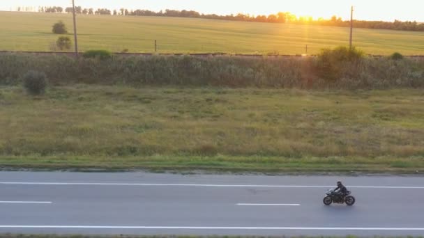 Мотоцикліст їздить на мотоциклі по сільській дорозі. Людина в шоломі їде на сучасному спортивному мотоциклі на шосе з сонцем на фоні. Хлопець їде на велосипеді під час подорожі. Концепція свободи. Вид з повітря — стокове відео