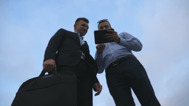 Dos jóvenes hombres de negocios hablando y usando tableta PC al aire libre luego adiós y divergen. Los hombres de negocios que trabajan en tableta digital exterior con el cielo en segundo plano. Colegas que aplican tecnología móvil — Vídeos de Stock