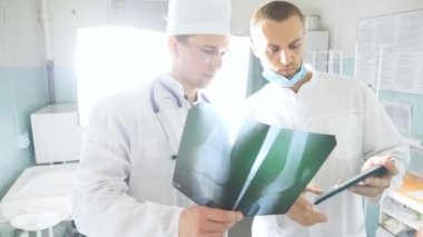 Hastanın röntgen görüntüsü hakkında birbirlerine danışırlarken tablet kullanan sağlık görevlileri. Hastanedeki tıp çalışanları röntgen izlerini inceliyor. Kafkasyalı iki doktor MRI fotoğrafına bakıp bunu tartışıyor.