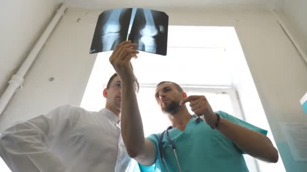 Les travailleurs médicaux à l'hôpital examinent les empreintes radiographiques. Deux médecins caucasiens regardent la photo IRM et en discutent. Médecins masculins se consultent tout en regardant l'image de rayons X. Gros plan — Video